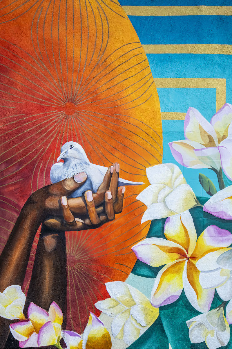 mural detail; painting of brown female hands holding a dove against a background of bright colors and flowers