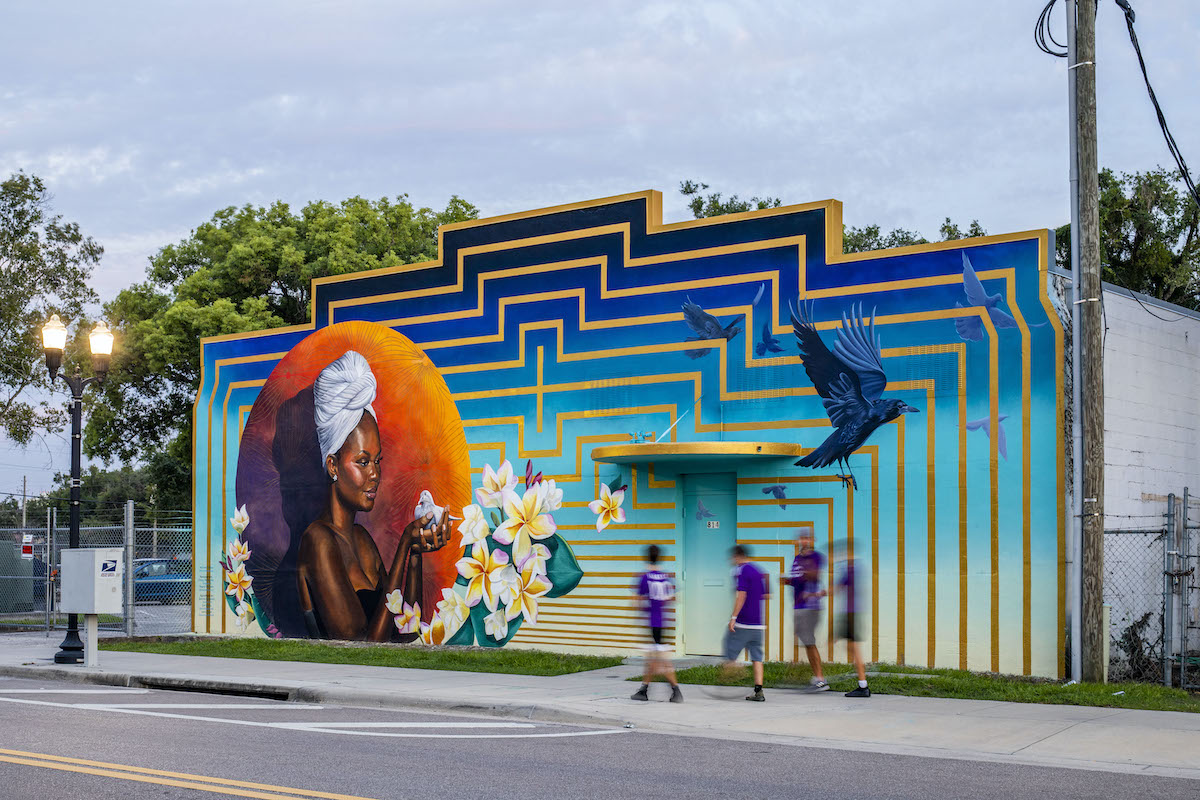 boys in purple jerseys walk past a mural in bright colors and featuring a Black woman holding a dove in her hands