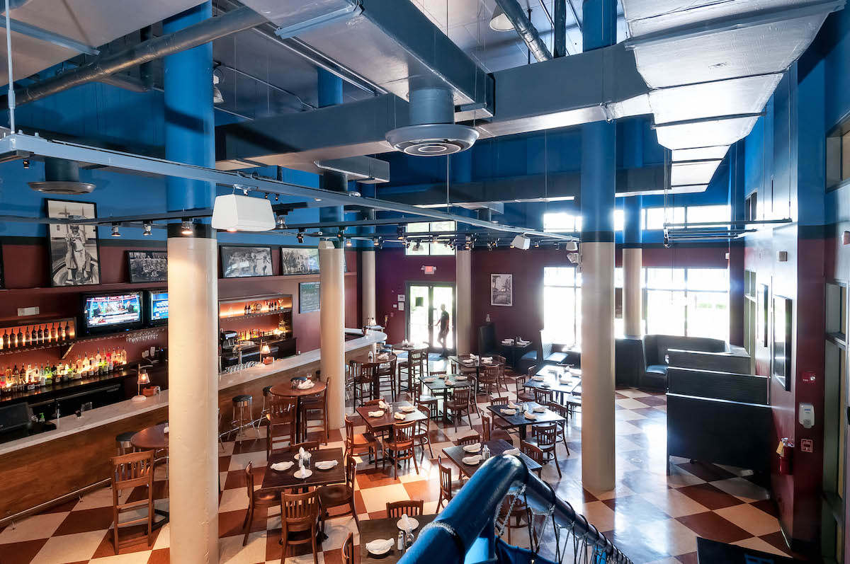 View from above of large restaurant with white pillars and checkerboard floor and large bar and large windows.