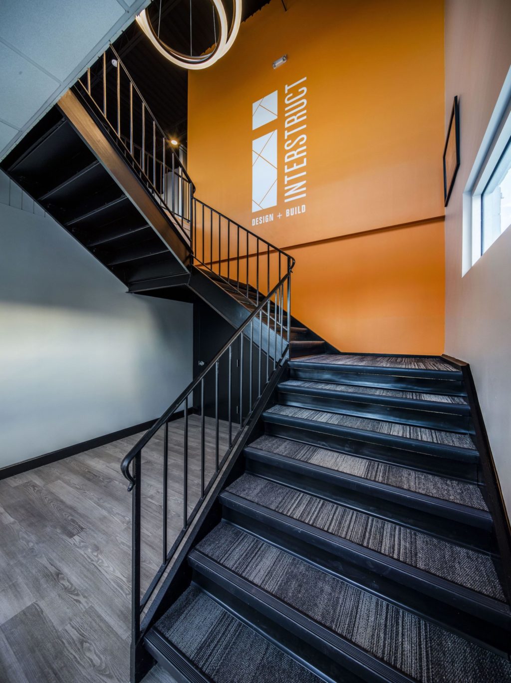 Split stairwell with large orange wall featuring signage for Interstruct Design + Build.